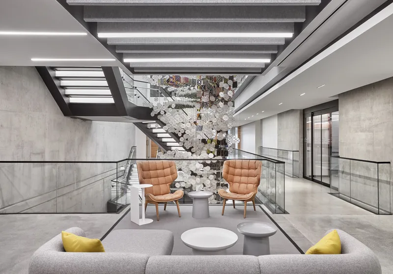 Multi-level atrium with floating steel stairs and a sculptural installation above tan leather seating