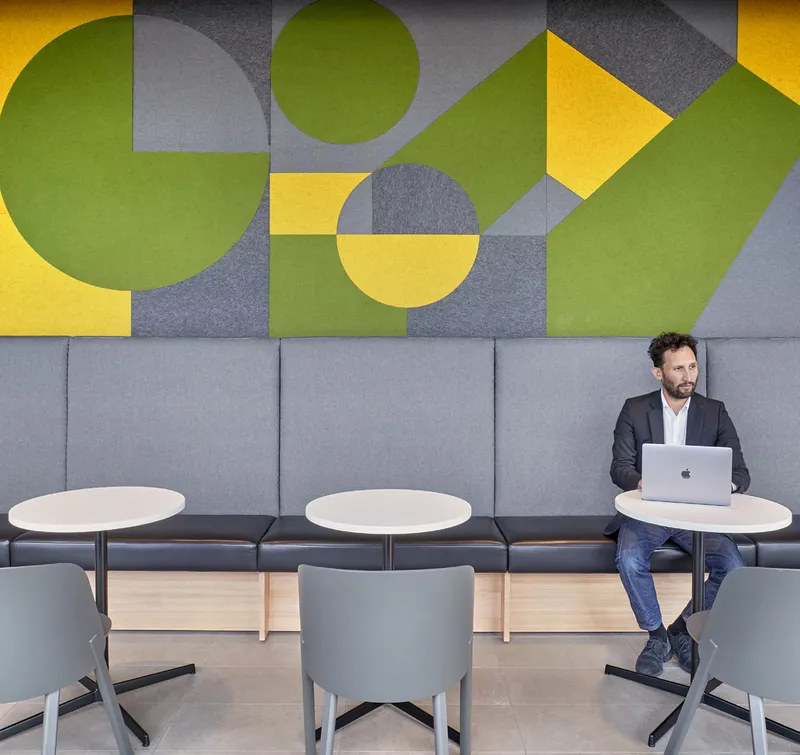 Lounge area with geometric yellow and green wall panels above a grey upholstered bench