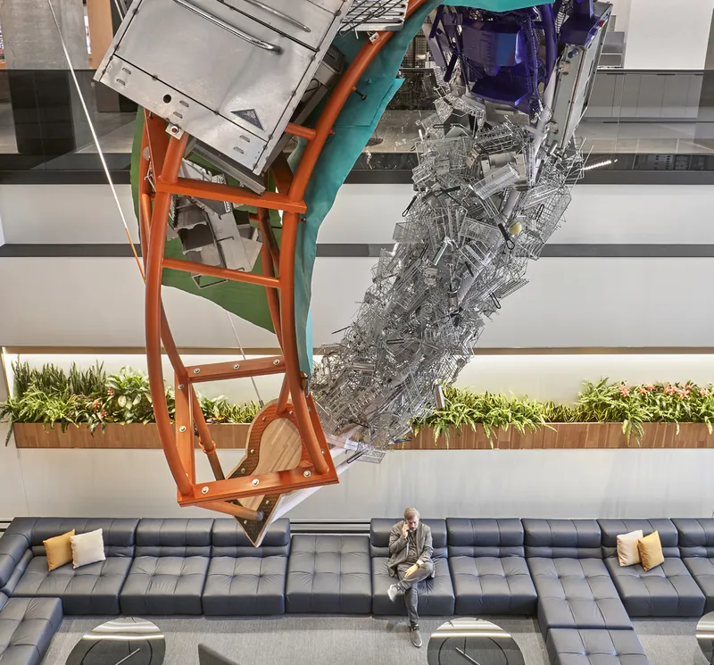 Double-height atrium with suspended sculptural installation above planted beds and modular seating