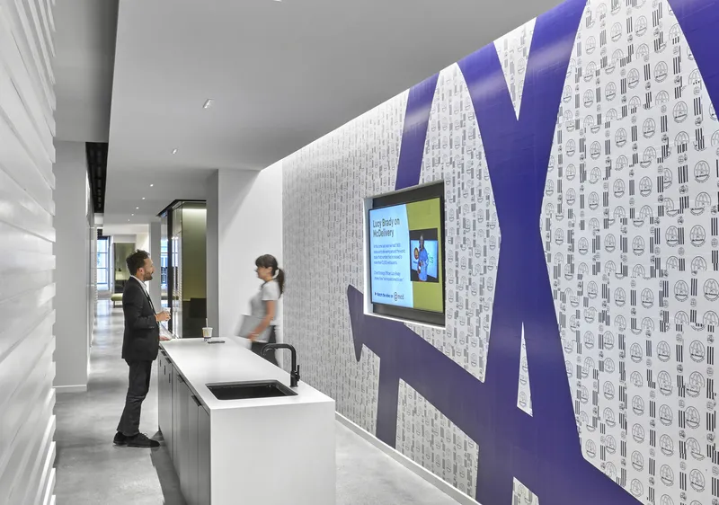 Corridor with patterned wallpaper featuring a large graphic letter and mounted digital screen