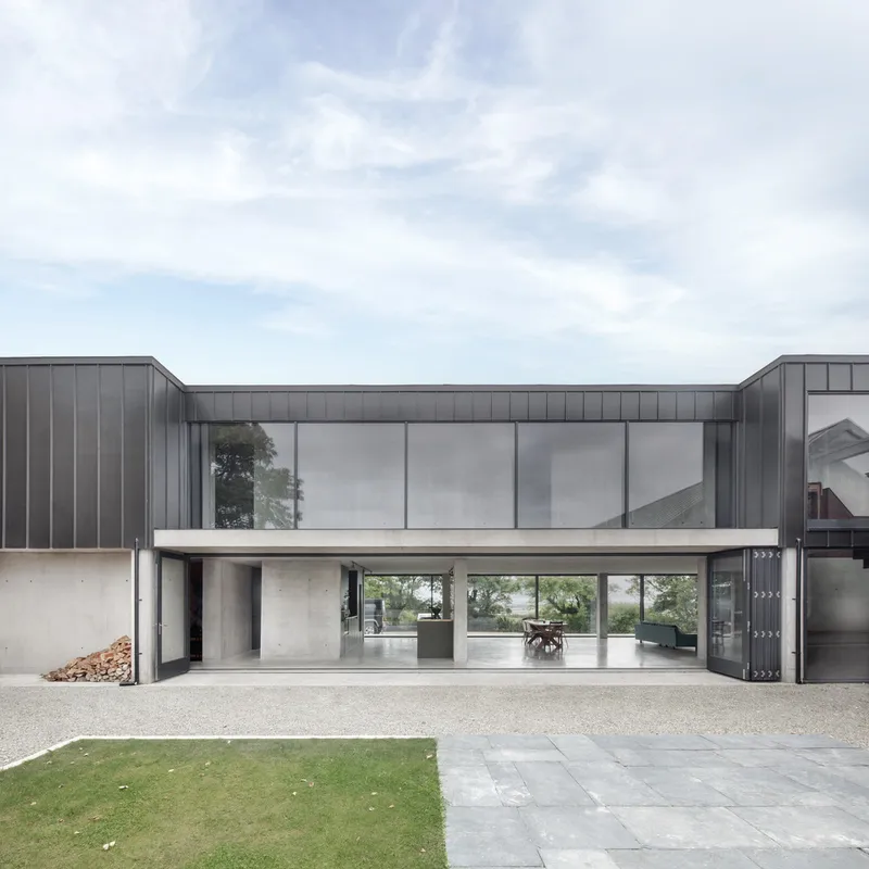 Front elevation showing the cantilevered upper volume with grey metal cladding above a recessed concrete ground floor