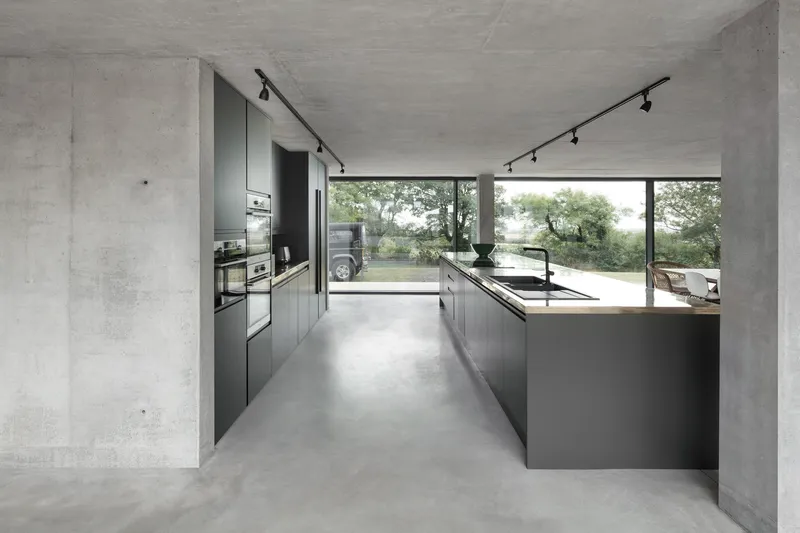 Kitchen with dark grey cabinetry and island beneath board-formed concrete ceiling and track lighting