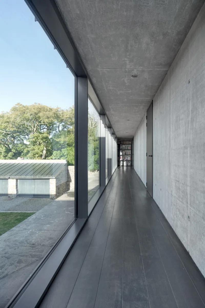 Corridor with floor-to-ceiling glazing on one side and board-formed concrete wall on the other