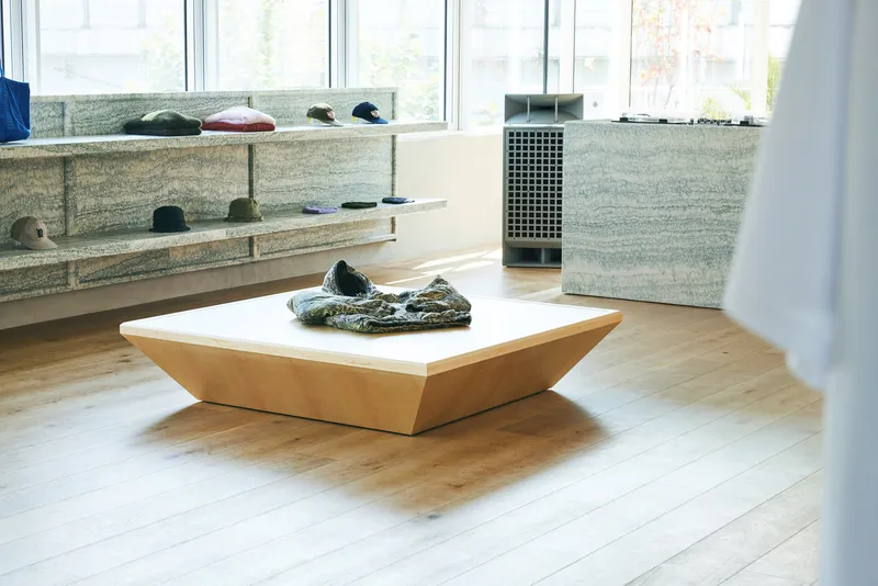 Through-view: wide corridor between two mirrored display rooms, white walls, hanging rails, figures browsing at far end