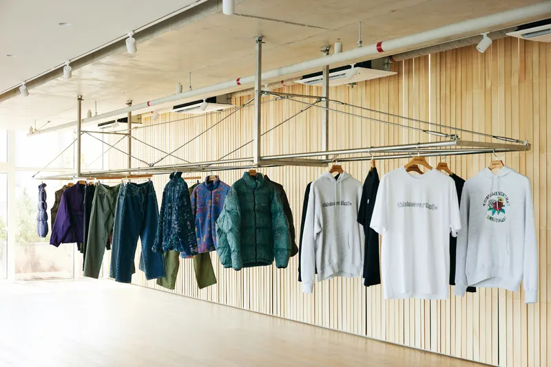 Hanging rail against timber: puffer jackets and sweatshirts on the tension-wire system, oak slat wall, concrete ceiling with exposed services