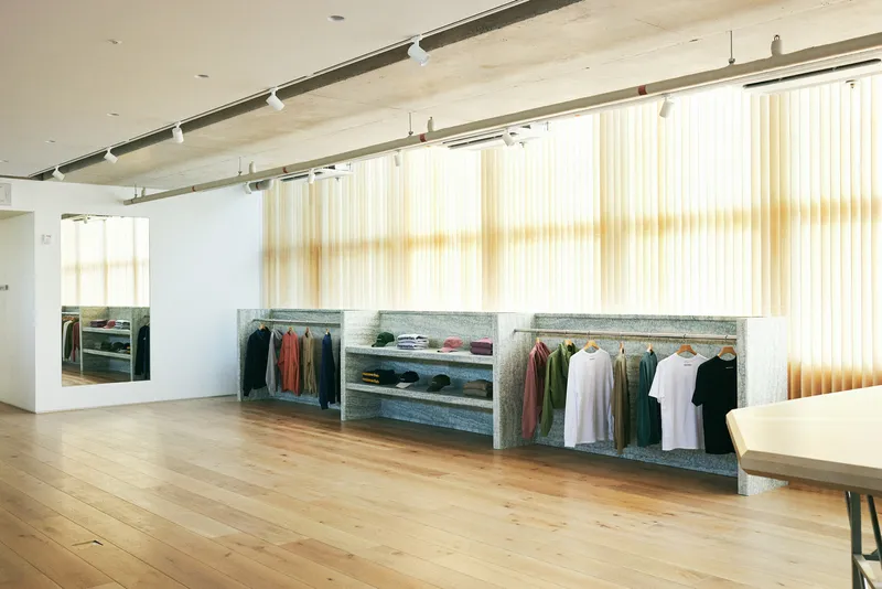 Clothing wall: garments hung on tension wire against granite stone wall, stepped shelves with folded items and accessories