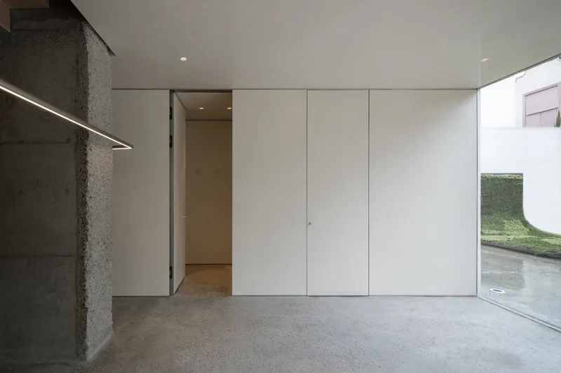 Interior detail: white flush panel doors, concrete column with exposed aggregate, LED linear light, glass corner window to garden