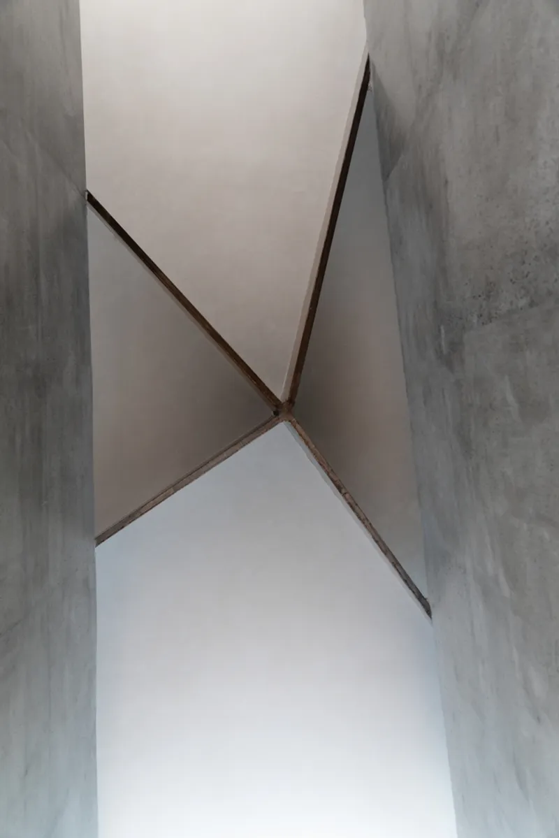 Ceiling detail: angular concrete planes meeting at a geometric fold, smooth plaster finish