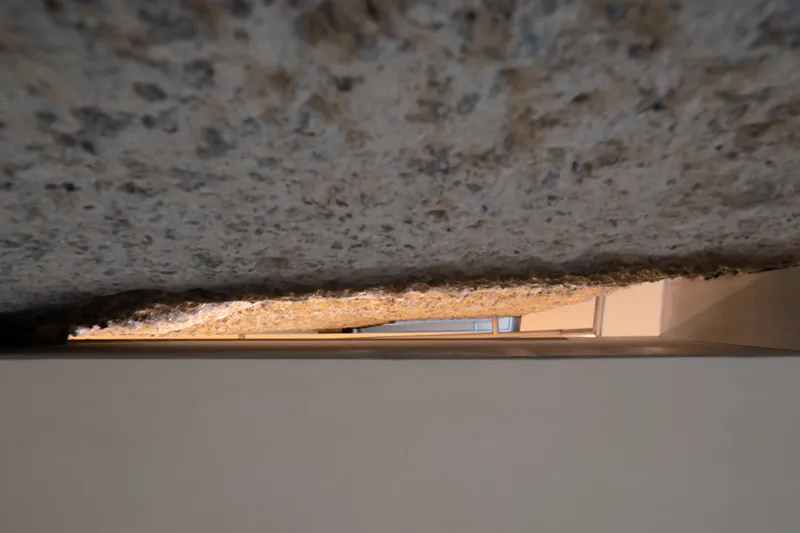 Soffit detail: rough granite underside of stair core, narrow gap revealing LED light and oak floor below