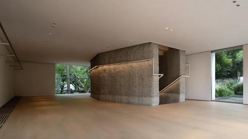 Ground floor: rough stone stair core with continuous LED handrail light, oak floor, frameless glass walls, garden trees outside