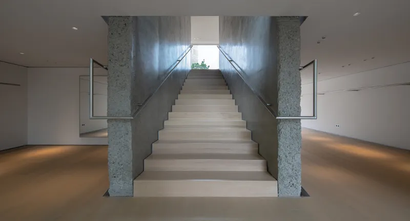 Staircase from below: wide white treads between rough granite columns, glass balustrade, daylight from above