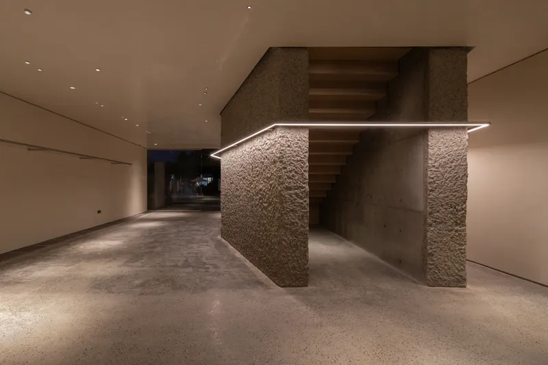 Lower level: rough stone stair core lit by LED strip along handrail, concrete floor, dark atmospheric lighting