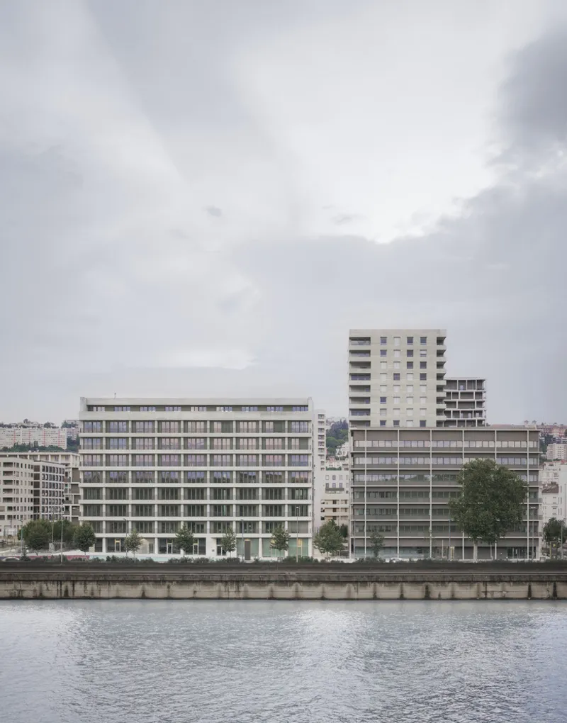 View across the waterfront showing the horizontal facade bands and adjacent residential towers under cloudy sky