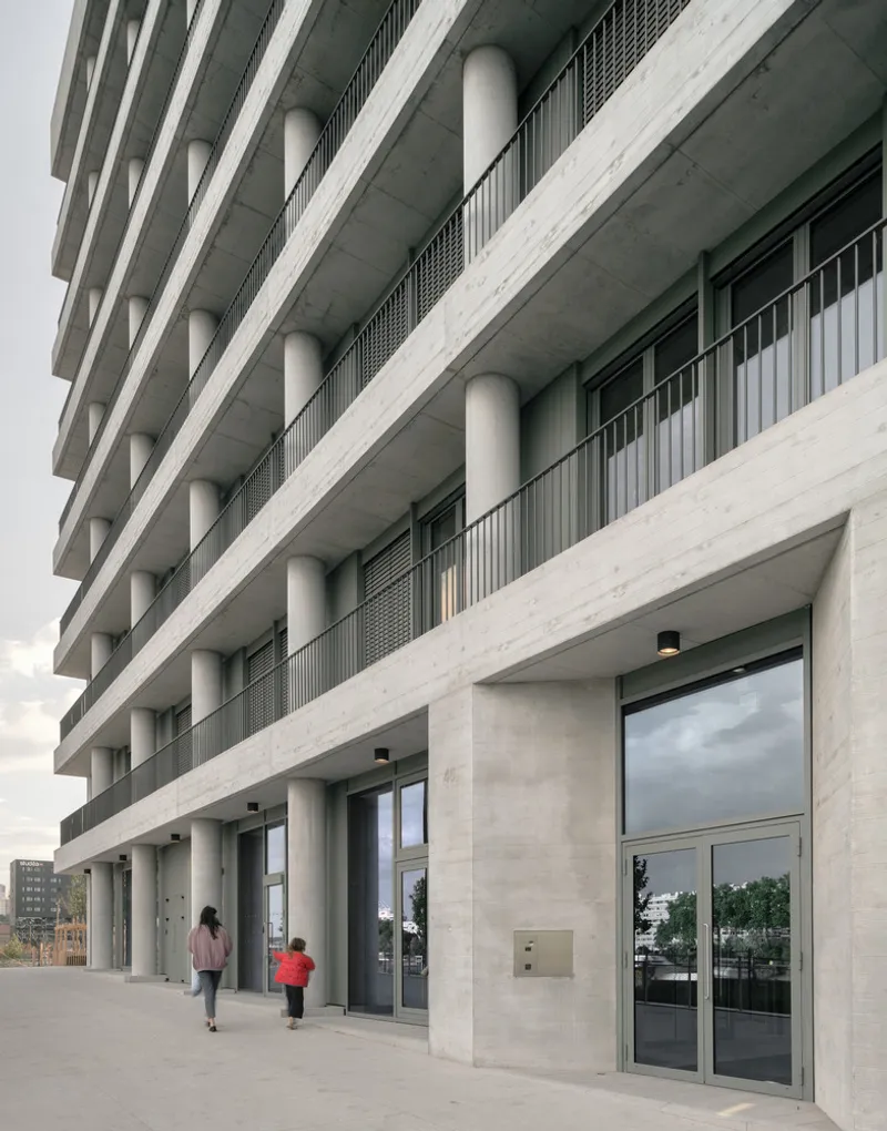 Ground-level colonnade with circular concrete columns and two pedestrians walking past glazed storefronts