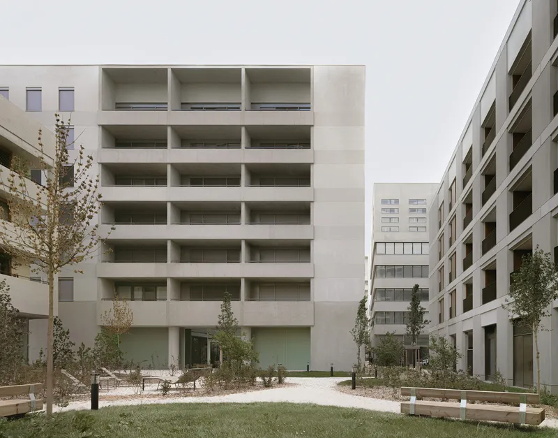 Courtyard view of the recessed balcony facade with young trees and wooden benches in autumn