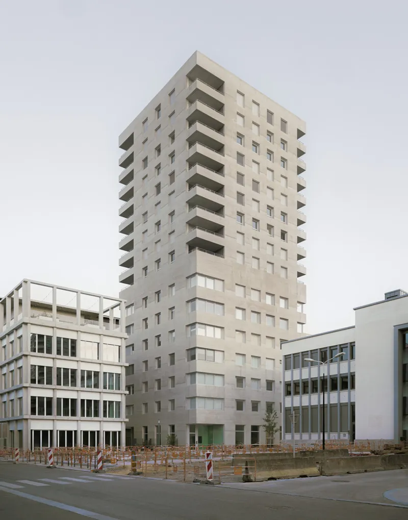 Corner view of the concrete tower with punched windows and projecting balconies under overcast sky