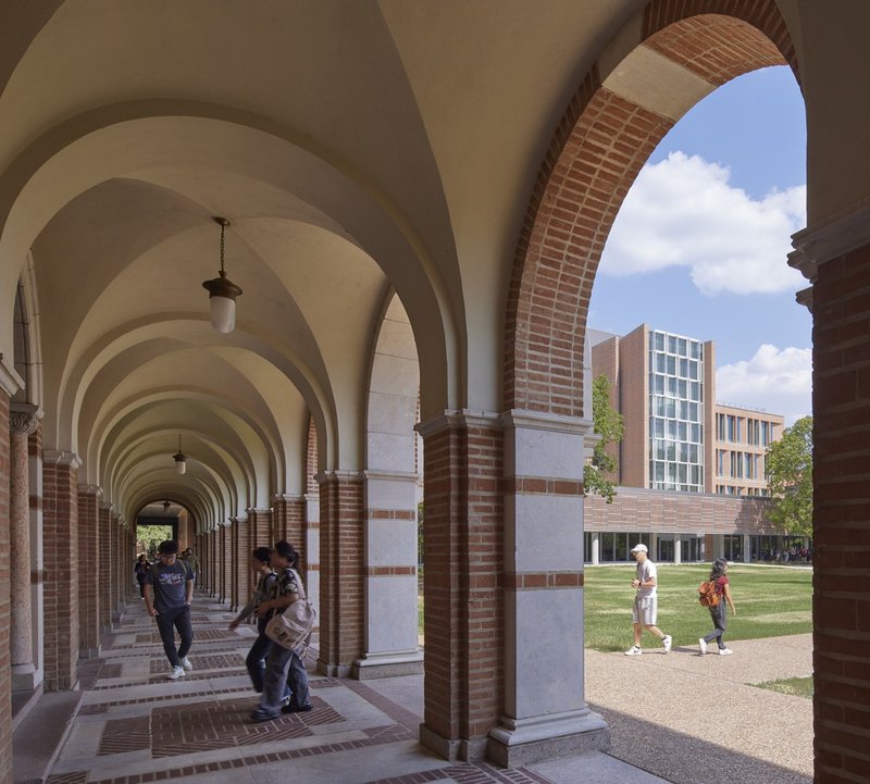 Vaulted arcade with brick and stone arches overlooking a green lawn and glazed building facade