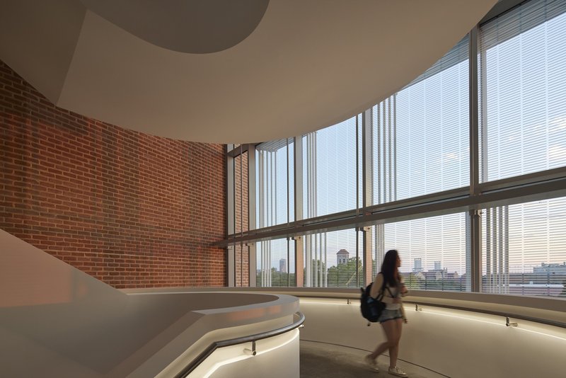 Curved interior hallway with exposed brick walls and floor-to-ceiling windows framing the city skyline