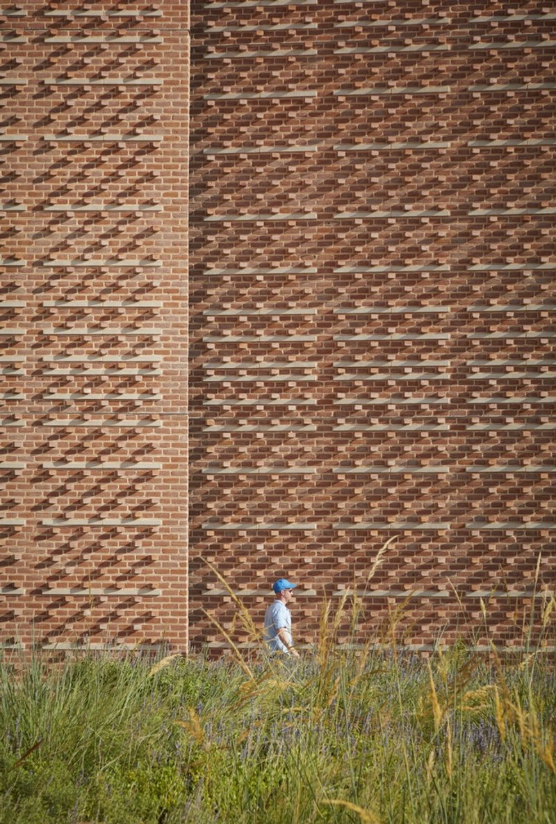 Brick facade with varied bond pattern behind tall grasses and person walking below