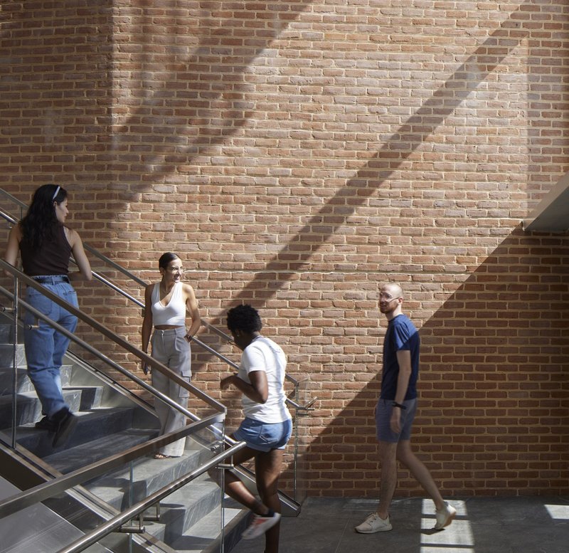 Brick wall with diagonal shadow patterns beside steel and concrete staircase with students gathered