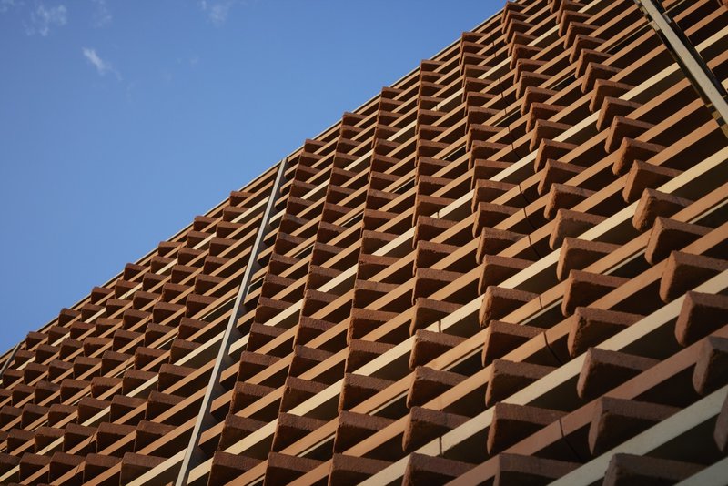 Upward view of terracotta louver screen in diagonal pattern against blue sky