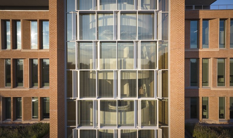 Central glass stair tower framed by brick wings with vertical window slots under clear sky