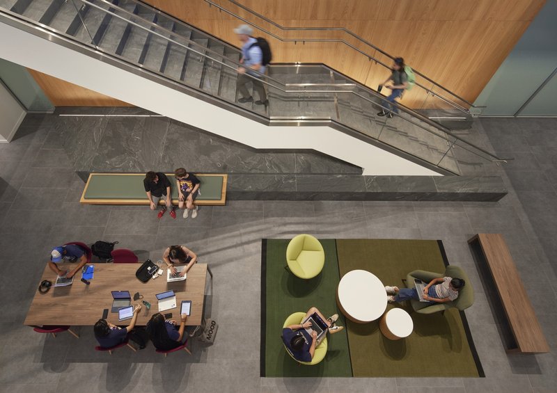 Top-down view of atrium lounge with circular seating on green carpet and students at timber table
