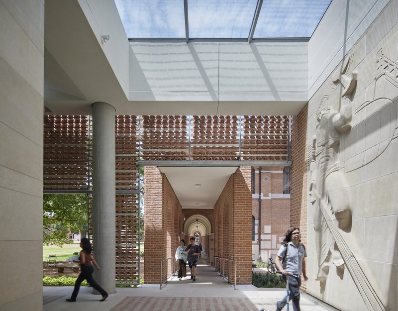 Skylit entrance passage framed by perforated brick screens and white stone walls with sculptural reliefs