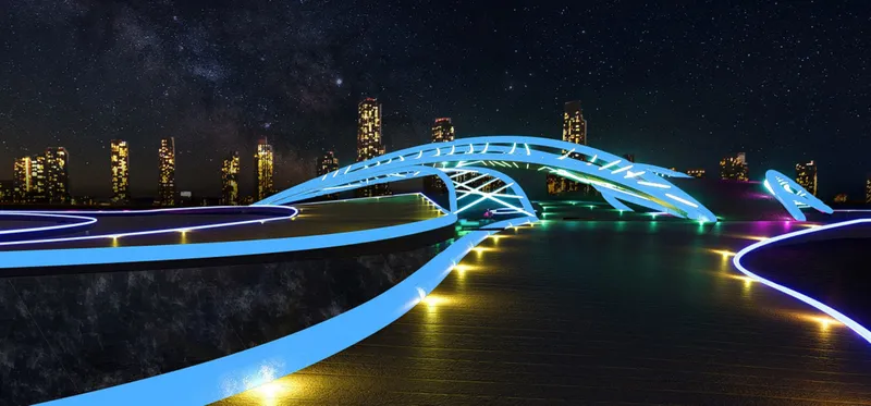 Long view of the illuminated bridge spanning a planted median with highrise towers in the background