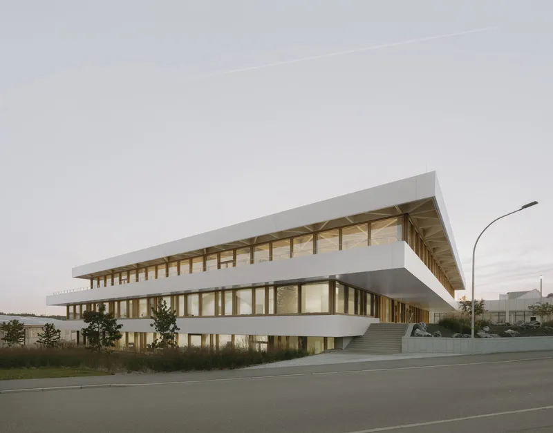 Streetview of the three-storey facade with timber columns and white horizontal bands at dusk