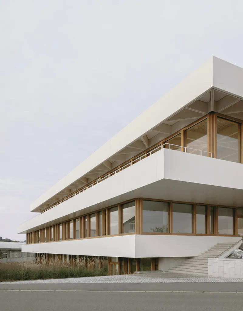 Close view of the cantilevered floors with timber structure beneath white parapets and overcast sky