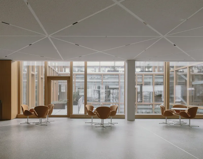 Interior lounge with tan leather chairs arranged beneath a faceted white ceiling and timber courtyard windows