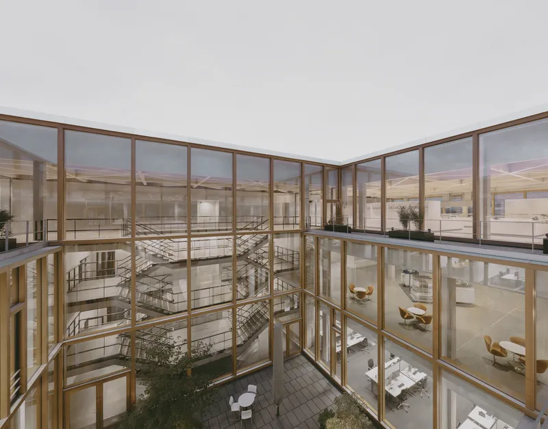 Corner view of the glazed atrium showing the spiral stair and multi-level interior at twilight