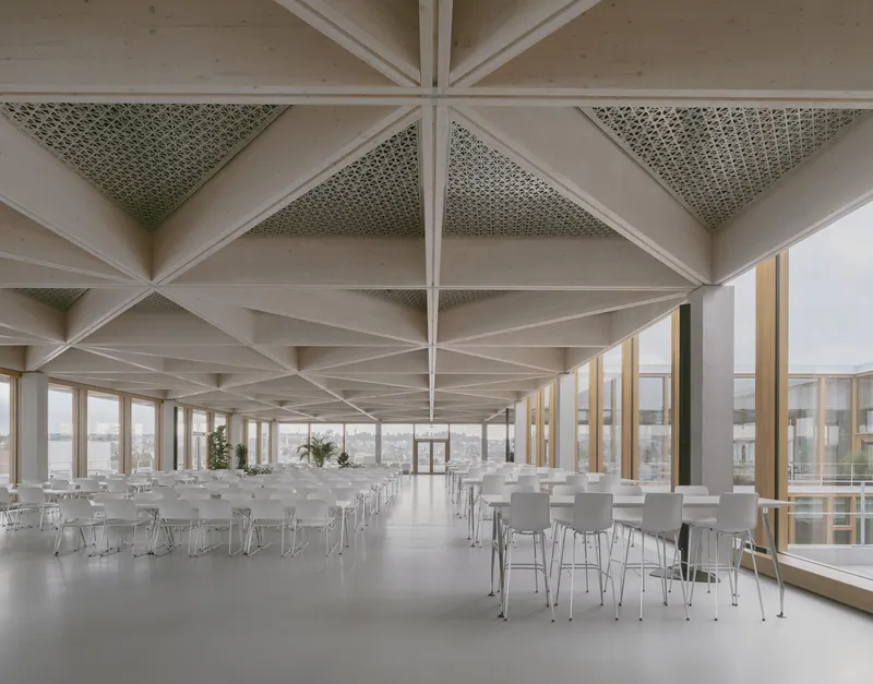 Interior dining hall with triangulated timber ceiling beams and perforated acoustic panels between exposed rafters