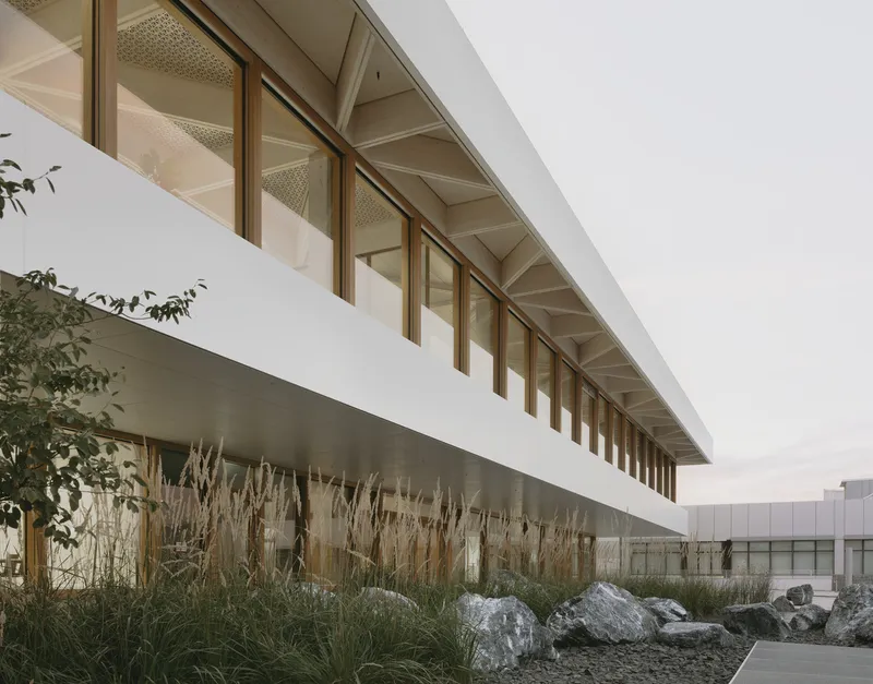 Elevated walkway with timber-framed windows spanning above a landscape bed of dried grasses and boulders