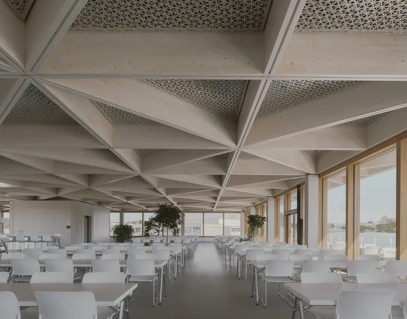 Dining hall with rows of white tables and chairs beneath a coffered ceiling with timber-framed glazing