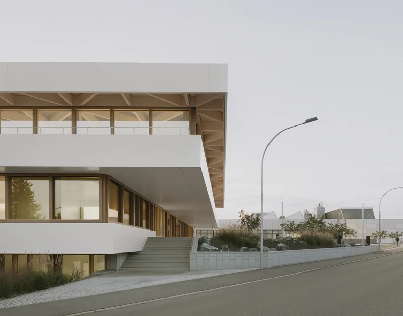 Street view of the stacked white volumes with recessed timber-framed glazing on an overcast day