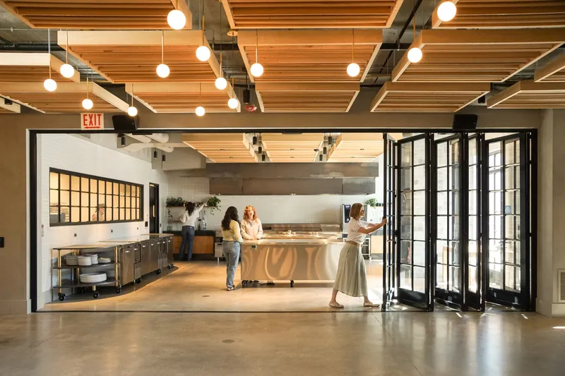 Ground-floor kitchen: timber beam ceiling, globe pendant lights, stainless steel counter, black bifold doors open to the dining room