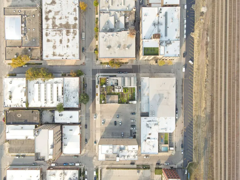 Aerial: the building in its Fulton Market block, rooftop farm and greenhouses visible, rail corridor at right, autumn trees