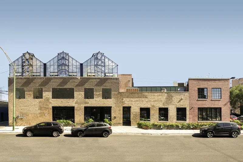 Street facade: original brick and limestone warehouse with three steel-and-glass greenhouses rising above the roofline, parked cars