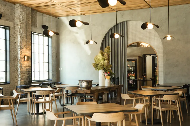 Restaurant dining: plaster arch with corrugated metal reveal, exposed brick, timber tables, pendant fan lights, warm evening tone