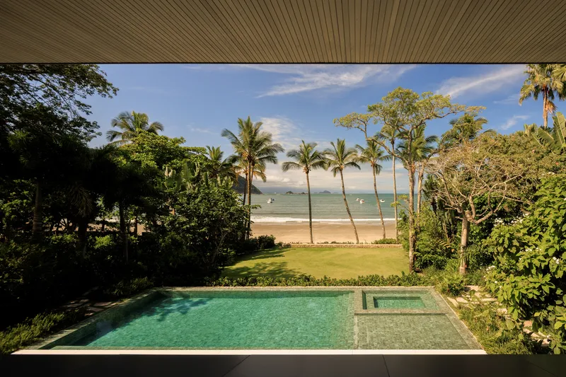 From under the roof: infinity pool, palm trees, beach and ocean visible beyond the garden, blue sky
