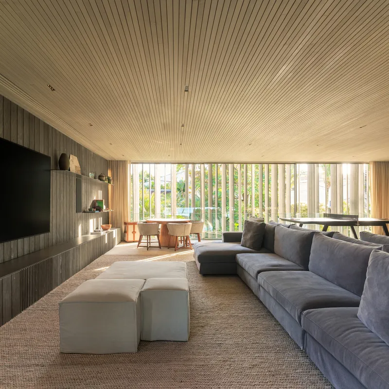Entertainment room: grey sectional sofa, timber ceiling, dark stone TV wall, timber brise-soleil windows, carpet
