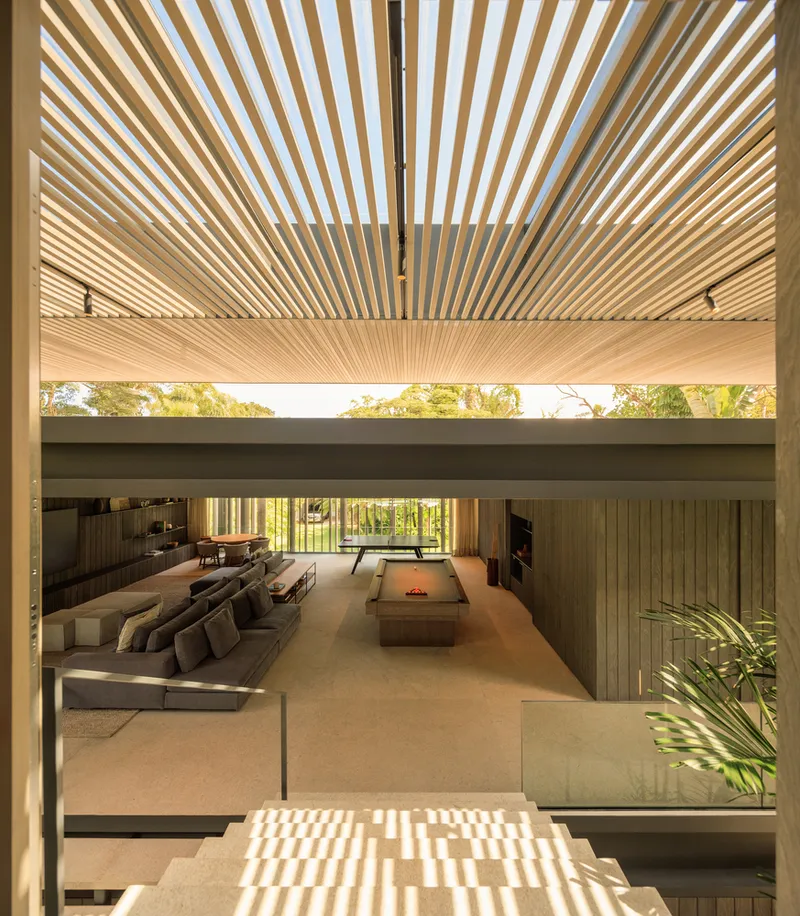 Interior: timber louvre ceiling filtering light, living area visible through the open plan, garden beyond