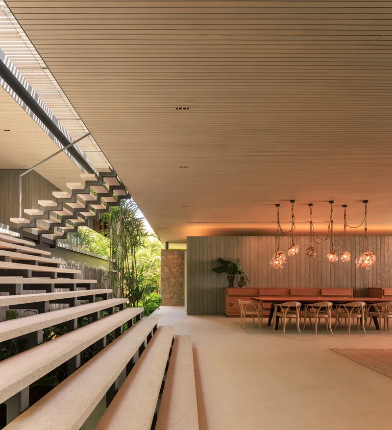 Dining area: floating stair rising behind, glass pendant cluster, timber table, timber-clad walls and ceiling