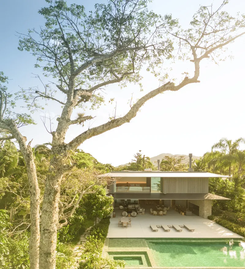From above: house with pool and sun loungers on stone terrace, tropical trees framing the view from the hillside