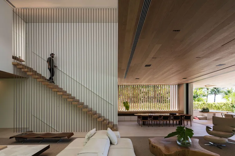Double-height living space with floating timber stair and vertical slatted wall with figure descending