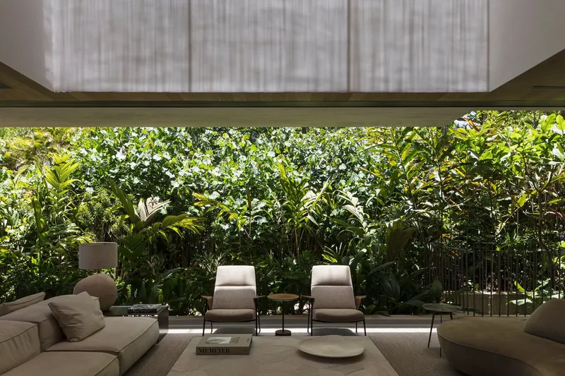 Interior view through horizontal window opening to layered garden planting beyond lounge seating