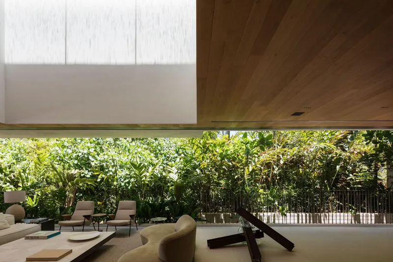 Covered living area with timber ceiling opening to a garden of dense foliage behind a metal fence