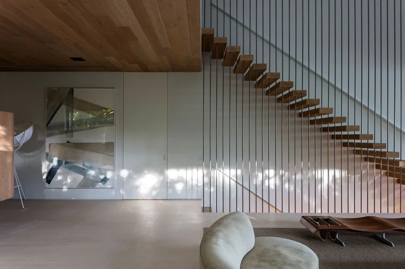 Cantilevered timber stair treads with wire railing and dappled sunlight on the white slat wall below